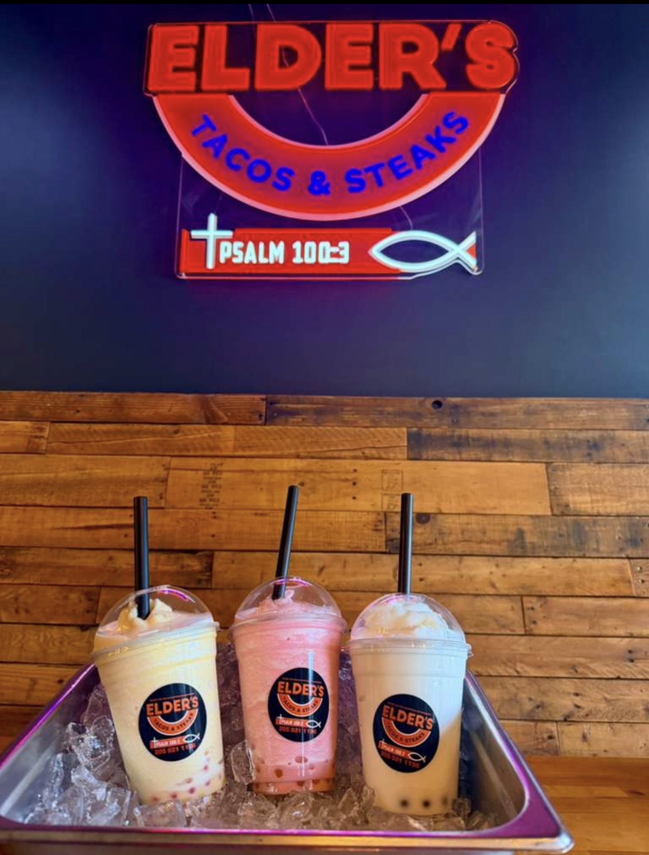 Three bubble teas on ice under the Elder's Tacos & Steaks neon sign