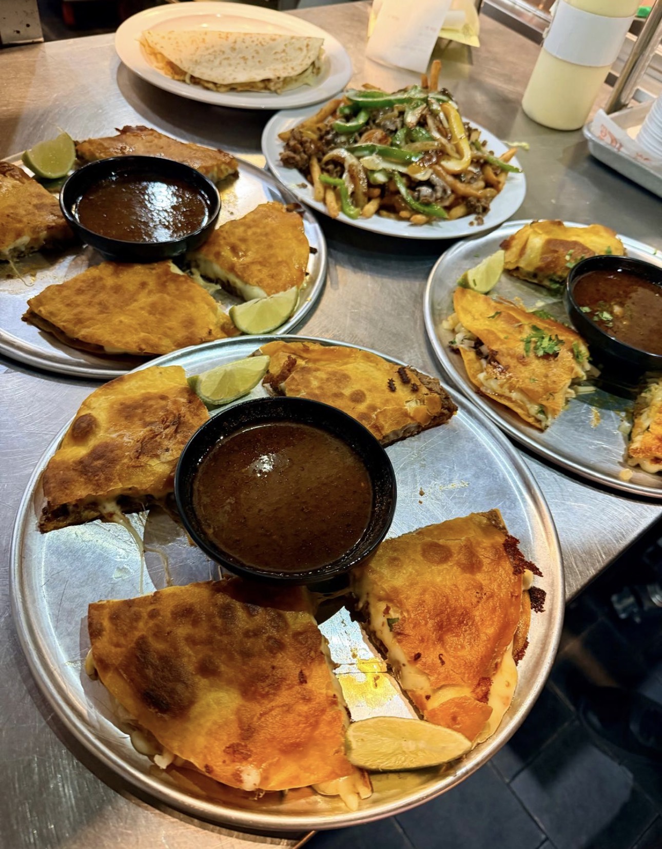 Three plates of birria quesadillas with consommé and Philly steak fries