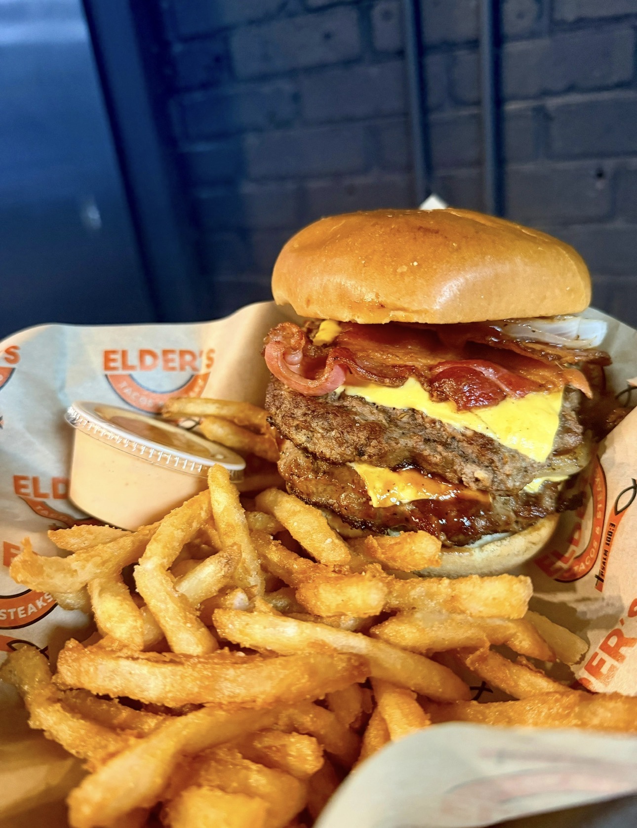 Double cheeseburger with bacon and crinkle-cut fries on Elder's Tacos & Steaks paper