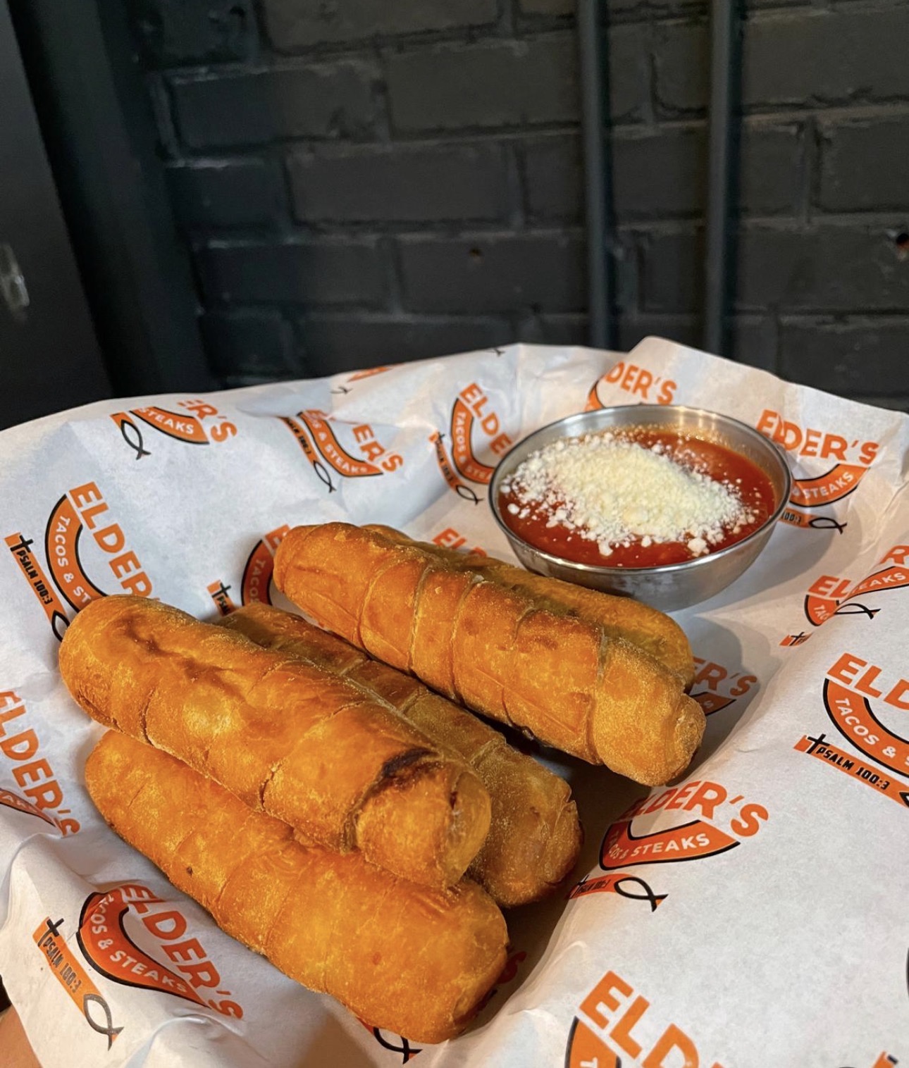Golden fried breadsticks with marinara and parmesan on Elder's paper