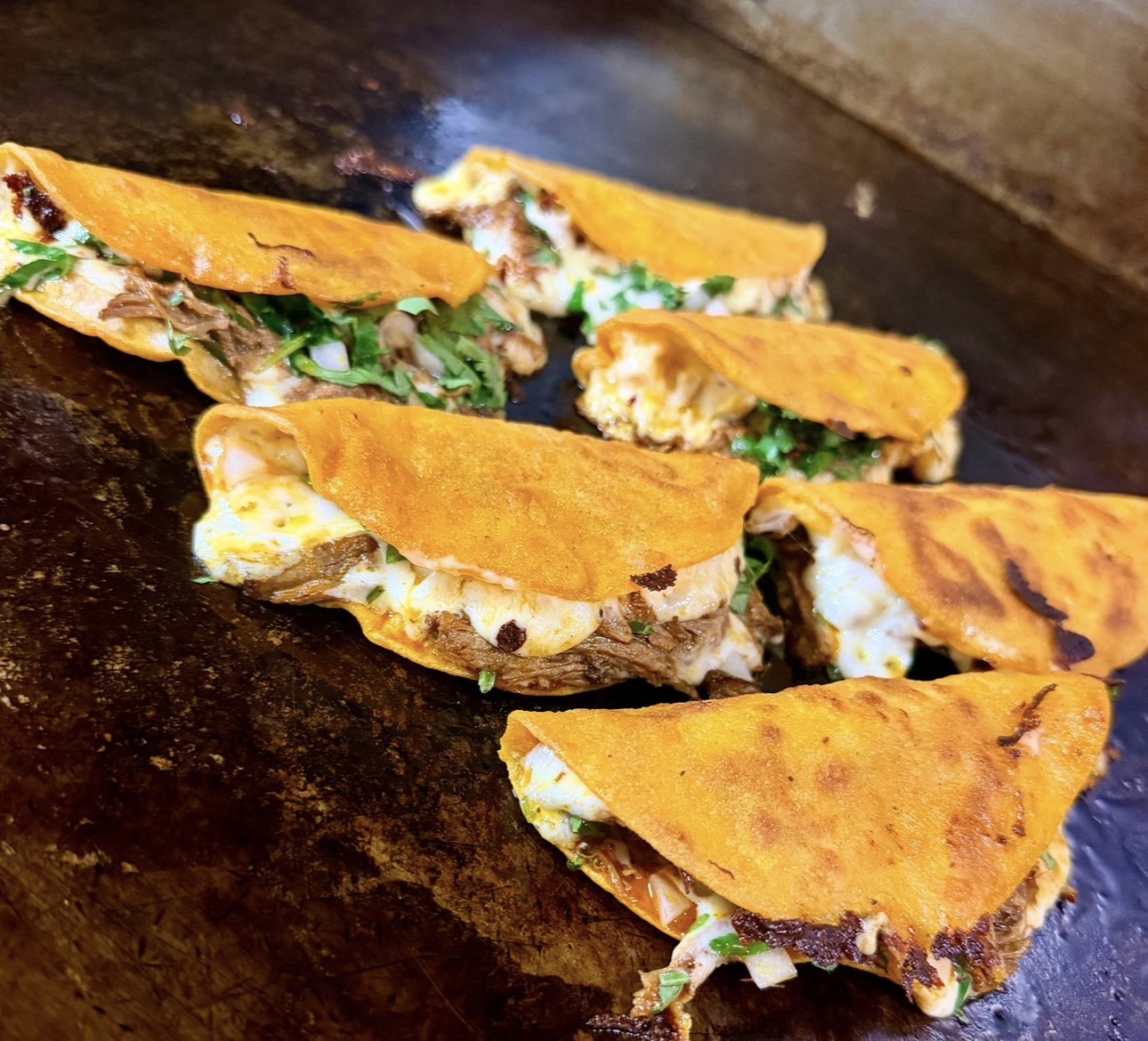 Birria quesadillas crisping on the griddle with cilantro and onion