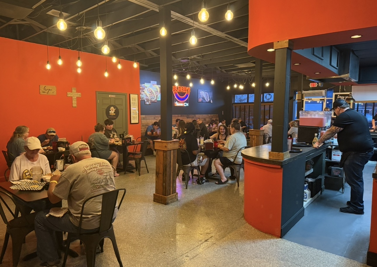 Busy dining room at Elder's Tacos & Steaks with orange walls, string lights and full tables