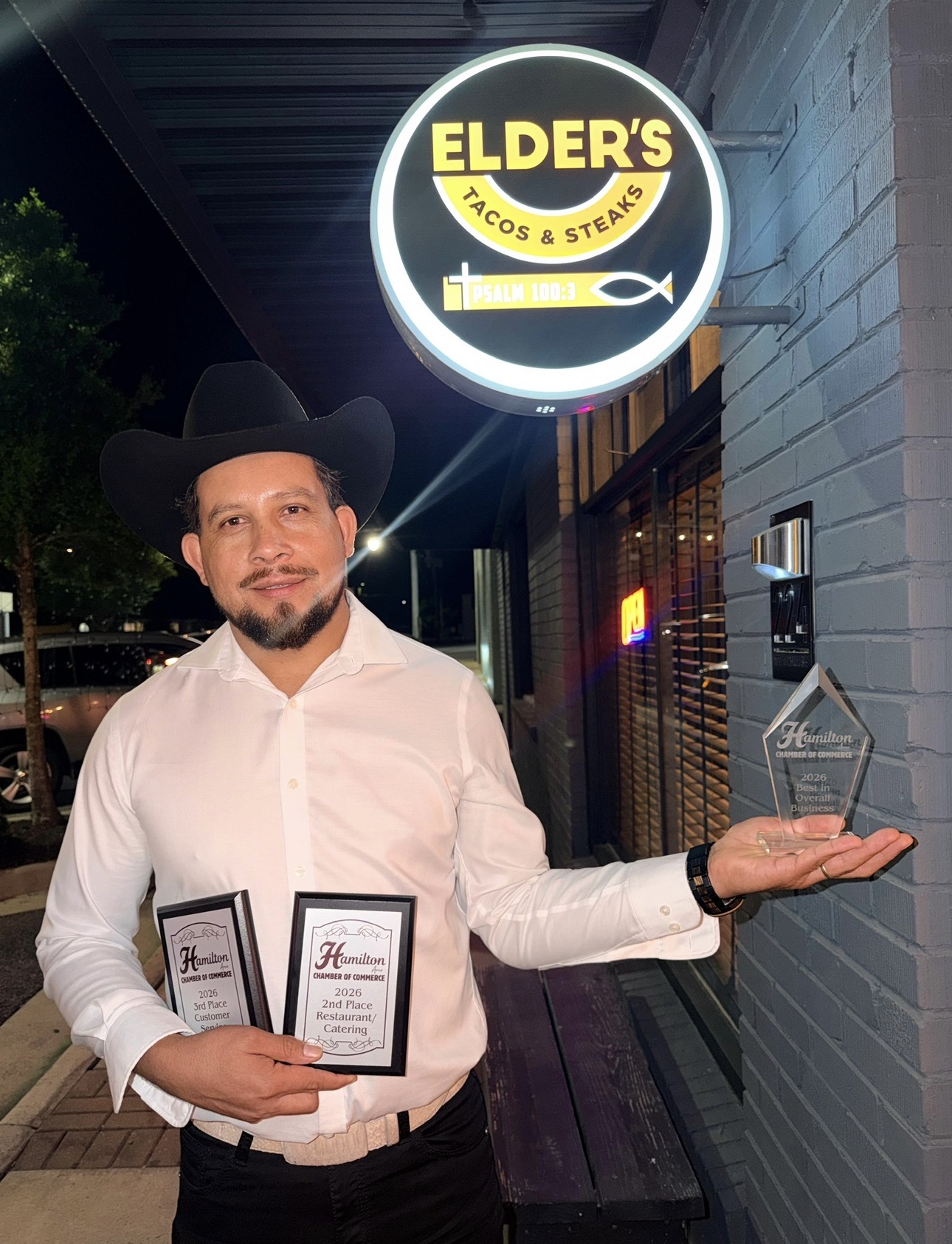Owner of Elder's Tacos & Steaks holding 2026 Hamilton Chamber of Commerce awards under the storefront sign