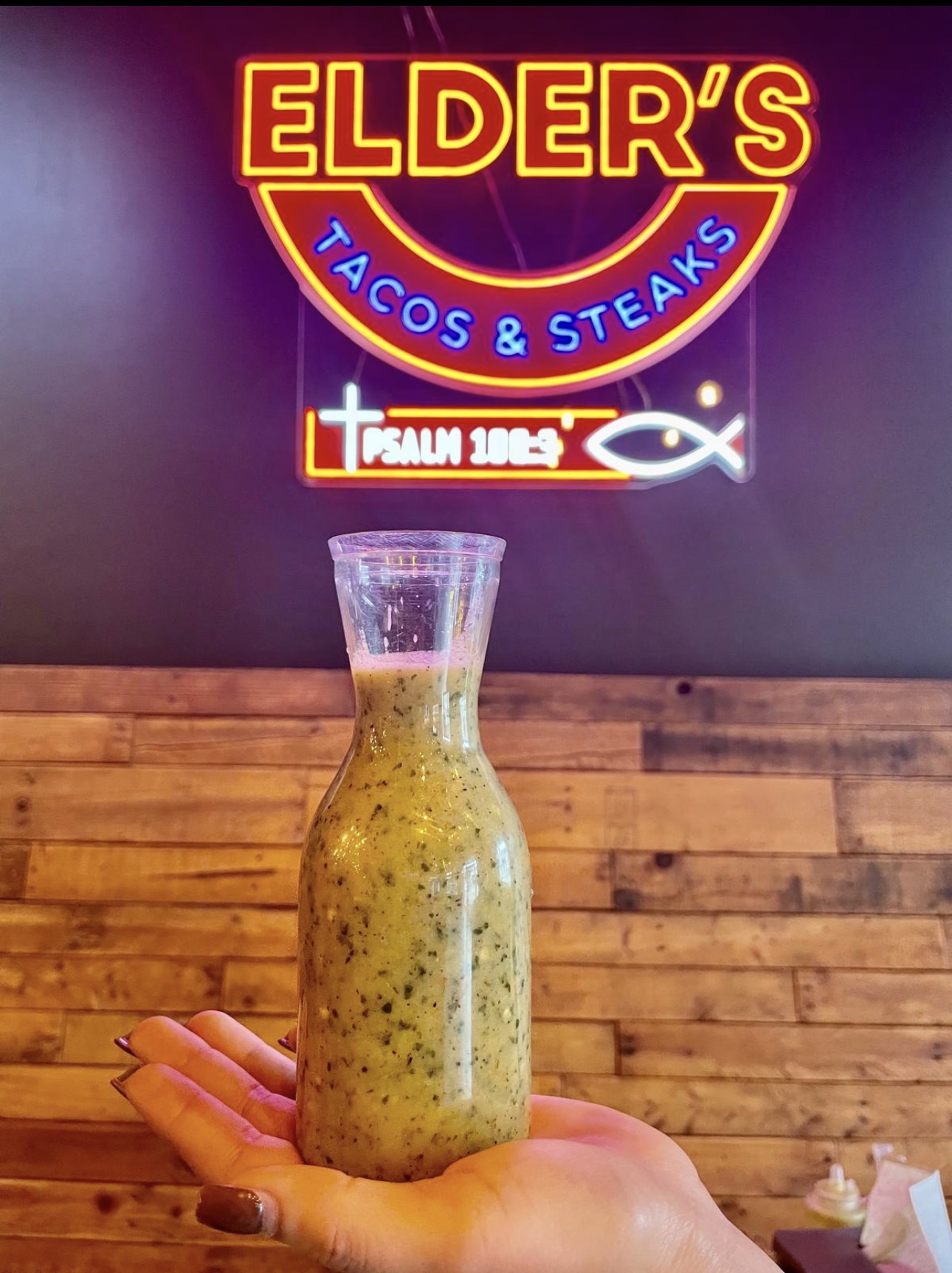 Fresh green salsa verde in a carafe under the Elder's Tacos & Steaks neon sign