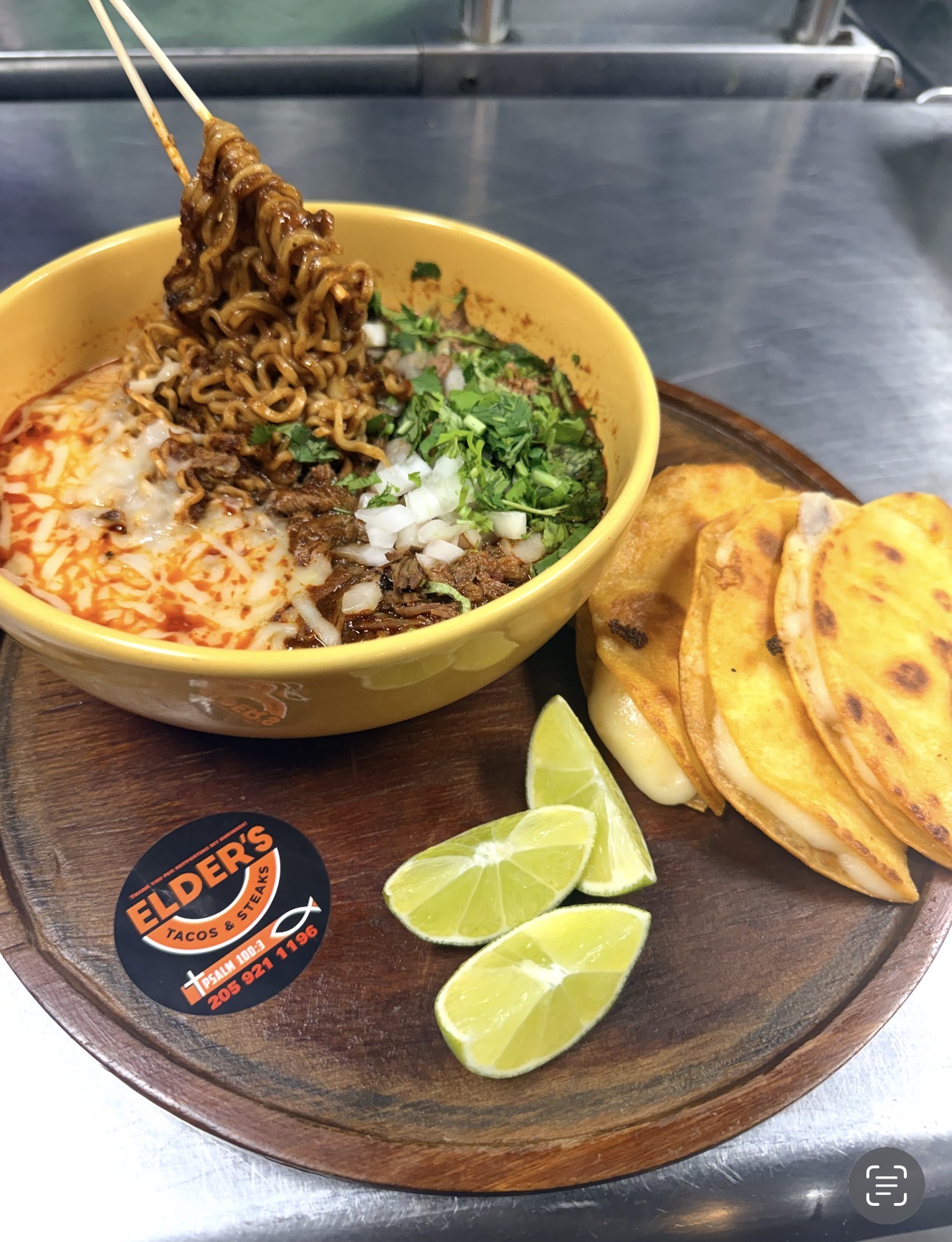 Birria ramen bowl with melted cheese, cilantro, onion, lime and crispy quesadillas at Elder's