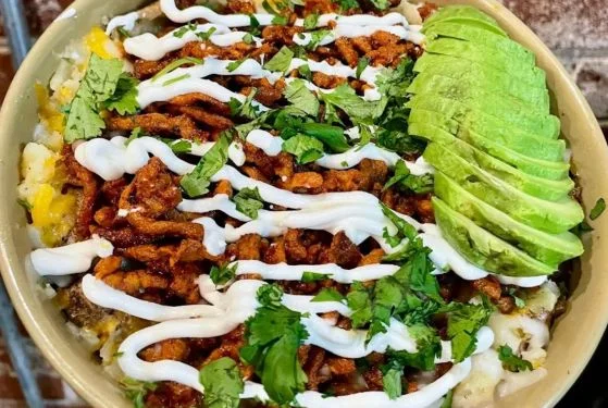 Burrito bowl topped with al pastor, crema, cilantro and avocado